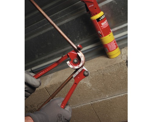 Pijpenbuiger in gebruik voor het buigen van een koperen pijp met een soldeerlamp op de achtergrond