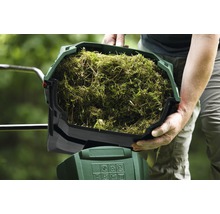 Persoon houdt een bak vol grasresten vast voor een tuinhakselaar.