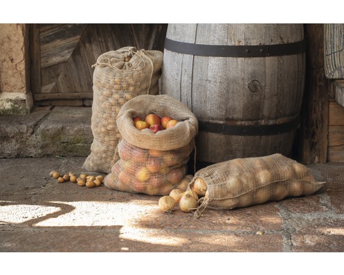 Jute zakken gevuld met appels, uien en aardappelen voor houten vat