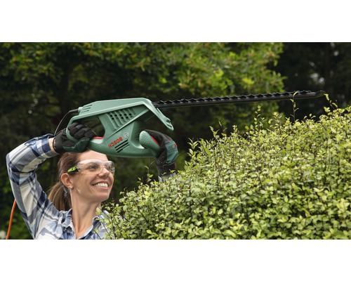 Vrouw snoeit heg met een elektrische heggenschaar van het merk Bosch.