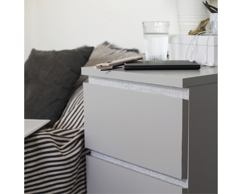 Grijs nachtkastje met lades, waarop een mobiele telefoon, een powerbank en een glas water staan.