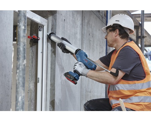 Een bouwvakker gebruikt een accuspuitpistool om een raam af te dichten.