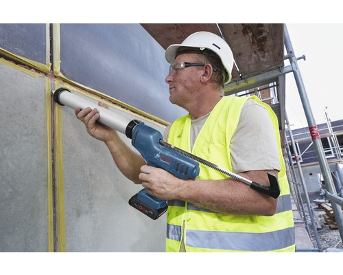 Vakman gebruikt een accukitspuit voor het afdichten van een muur op een bouwplaats.