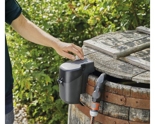 Watergeefautomaat op een regenton met slangaansluiting, bediend door een hand.