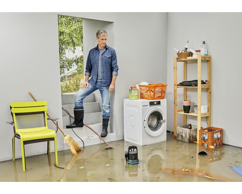 Overstroomde kelderruimte met man, wasmachine, meubels en dompelpomp