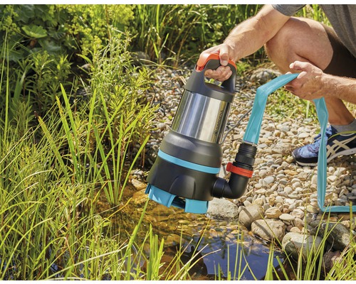 Een persoon houdt een Gardena dompelpomp voor vuil water met aangesloten slang boven een vijver