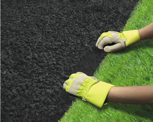 Twee handen met werkhandschoenen leggen mulch naast kunstgras.