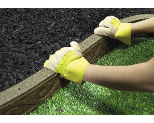 Een persoon met handschoenen legt een gazonrand tussen rubbergranulaat en kunstgras.