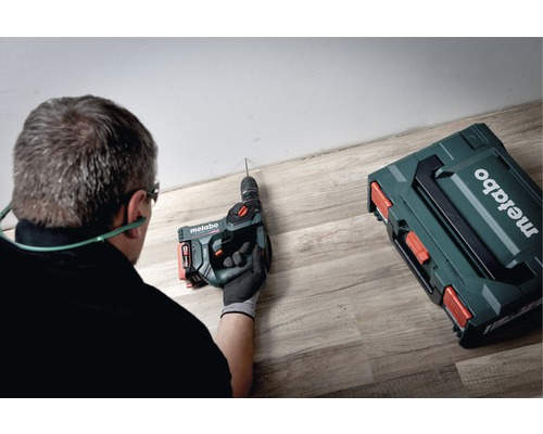 Ambachtsman boort met een Metabo boorhamer een gat in het plafond naast een Metabo gereedschapskoffer.