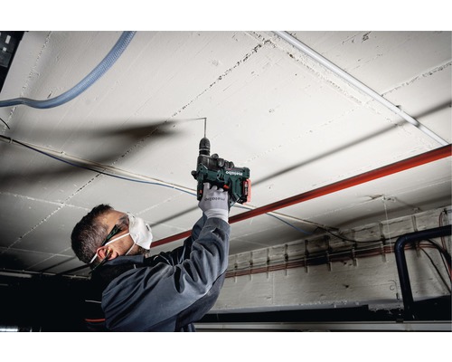 Een man boort met een boorhamer in een betonnen plafond.