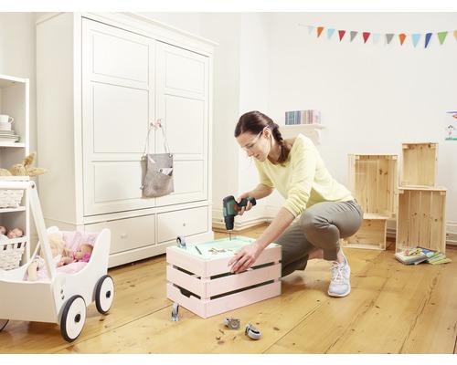 Vrouw boort schroef in houten kist in lichte kinderkamer