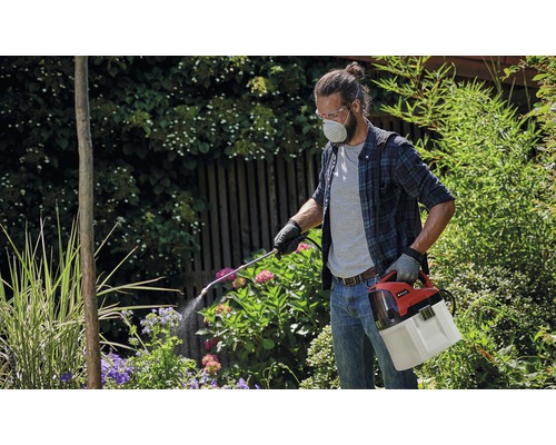 Man met veiligheidsbril en ademhalingsmasker die een accub plantsprayer in de tuin gebruikt.