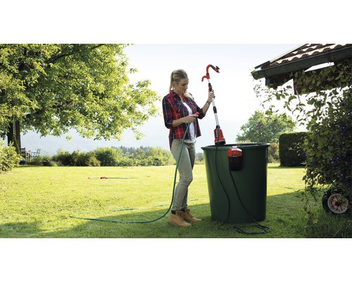 Vrouw bedient een telescopische tuinsproeier om planten in de tuin water te geven.