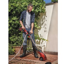 Man gebruikt een accu-voegenborstel in de tuin om onkruid tussen stenen te verwijderen.