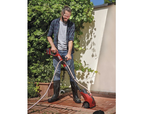 Man gebruikt een accu-voegenborstel in de tuin om onkruid tussen stenen te verwijderen.