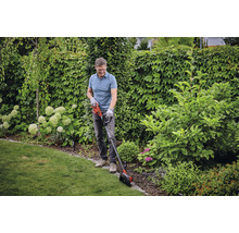 Man snoeit gazonranden met een gazontrimmer in de tuin.