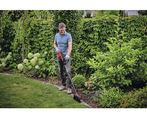 Man snoeit gazonranden met een gazontrimmer in de tuin.