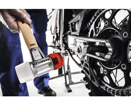 Een man gebruikt een hamer om aan een motorfiets te werken.