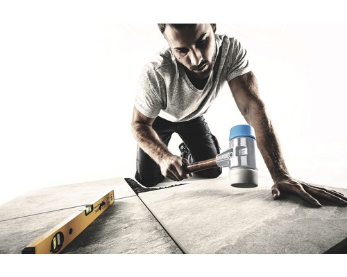 Ambachtsman legt tegels met rubberen hamer en waterpas