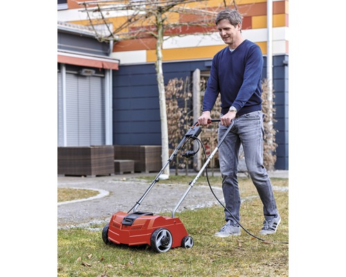 Een man gebruikt een elektrische verticuteermachine in de tuin om het gazon te verzorgen.