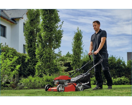 Man bedient een rode Einhell benzine grasmaaier in de tuin.