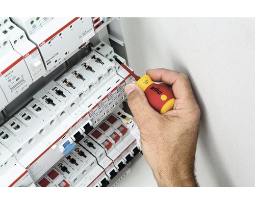 Een hand gebruikt een schroevendraaier op een zekeringkast met ABB-componenten.