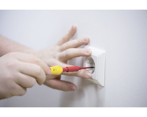 Een hand voert met een schroevendraaier elektrische werkzaamheden uit aan een stopcontact.