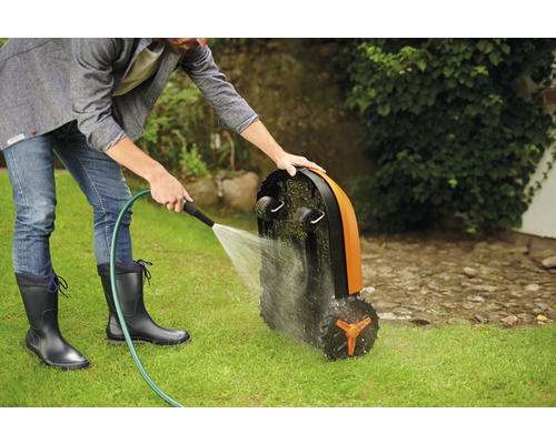 Een man reinigt een gazonrobot met een waterslang op een gazon.