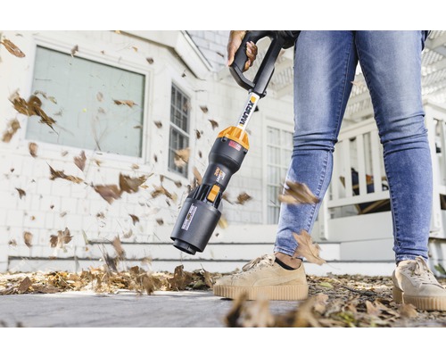Een persoon gebruikt een draadloze bladblazer om bladeren van een trottoir te verwijderen.
