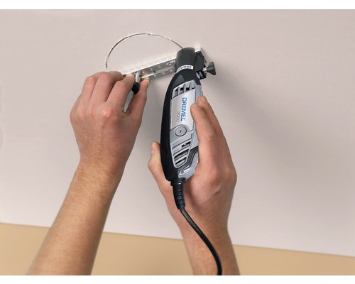 Iemand snijdt met een Dremel multifunctioneel gereedschap een gat in een plafond.