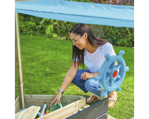 Vrouw speelt met zandspeelgoed in een zandbak met zonnescherm