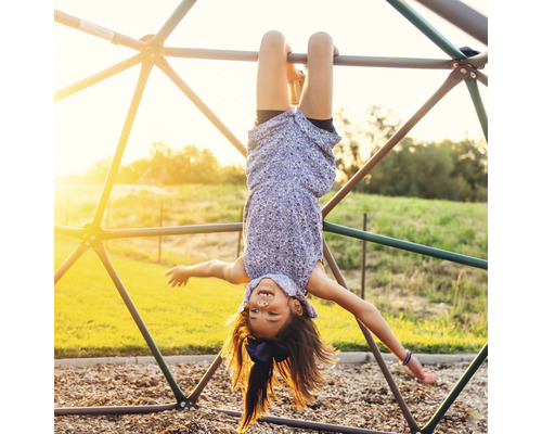 Meisje hangt ondersteboven aan een klimrek buiten.