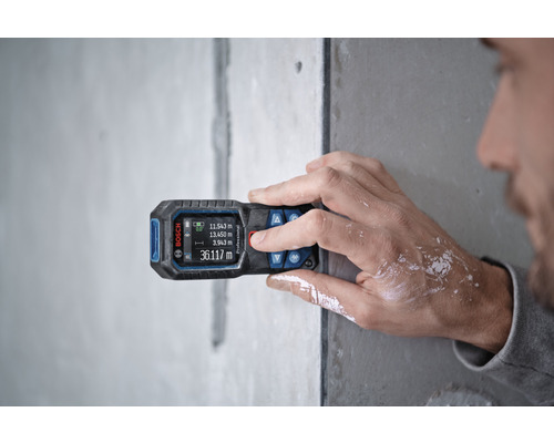 Een persoon gebruikt een Bosch afstandsmeter op een muur voor metingen.