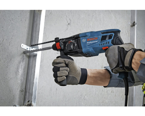 Een persoon boort een gat in een muur met een Bosch boorhamer.