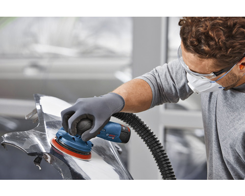 Een man schuurt een metalen werkstuk met een excentrische schuurmachine.