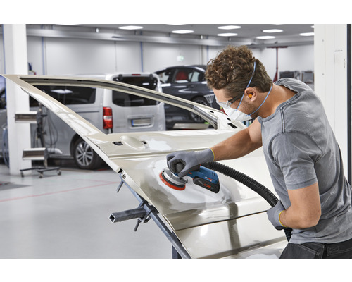 Een man schuurt een autodeur met een schuurmachine in een werkplaats.