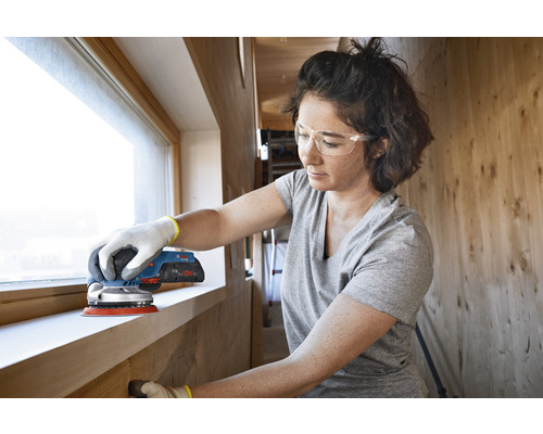 Vrouw schuurt raamkozijn met een excentrische schuurmachine
