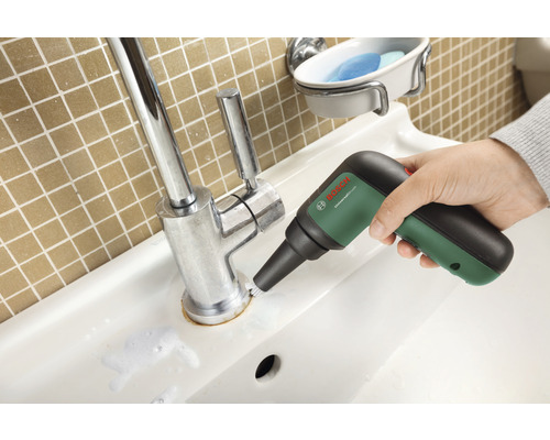 Een wastafel wordt schoongemaakt met een elektrische reinigingsborstel. Op de achtergrond een muur met vierkante tegels.