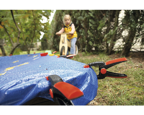 Afdekzeil met klemmen in de tuin, kind op loopfiets op de achtergrond