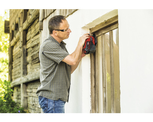 Een man met veiligheidsbril renoveert een houten raam met een multifunctioneel gereedschap.