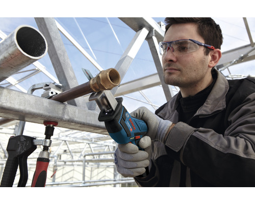 Een man zaagt een pijp met een Bosch reciprozaag, terwijl hij een veiligheidsbril en handschoenen draagt.