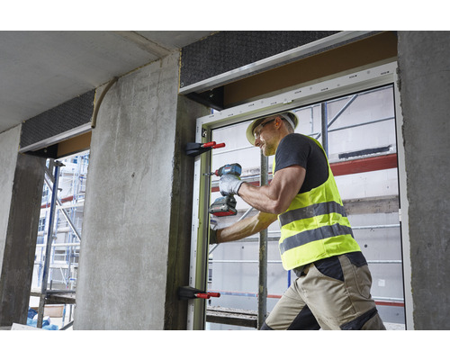 Een vakman monteert met een accuschroevendraaier een raam in een gebouw.