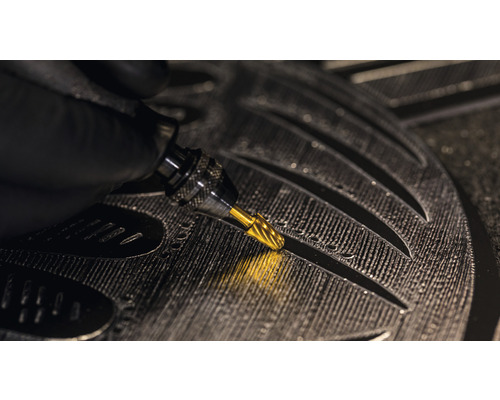 Close-up van een hand met een graveerstift die details in een werkstuk graveert.