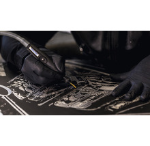 Detailopname van een persoon die met een Dremel gravures in een donker oppervlak aanbrengt