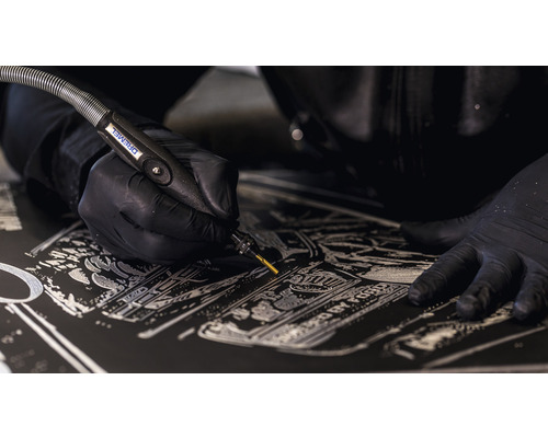 Detailopname van een persoon die met een Dremel gravures in een donker oppervlak aanbrengt
