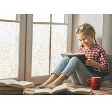 Meisje leest boek op vensterbank met raamfolie, kop en andere boeken