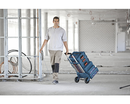 Ambachtsman trekt een gereedschapskofferwagen van Bosch door een bouwplaats.