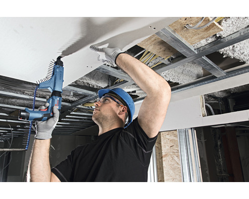 Een man bevestigt een gipsplaat aan een plafondconstructie met een gipsplaatschroevendraaier.