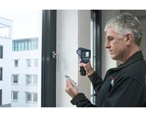 Man gebruikt een warmtebeeldcamera om een raam te analyseren.