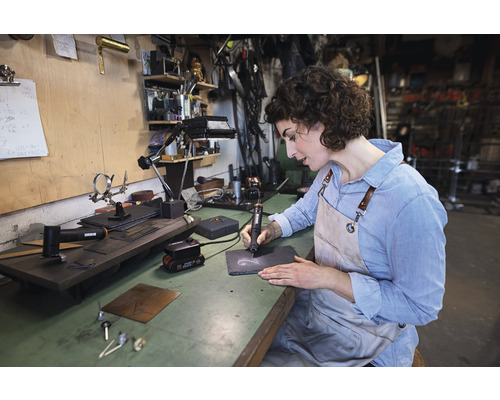 Vrouw graveert leisteenplaat met graveergereedschap op werkbank